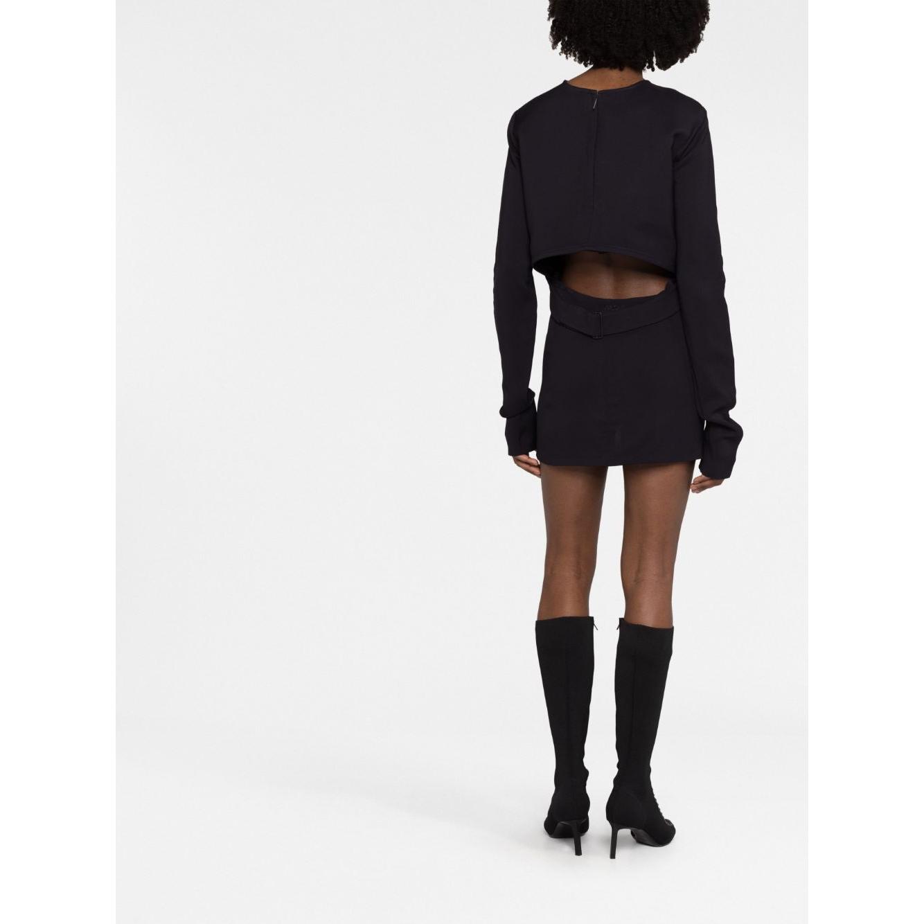 Back view of model wearing 032C black structured short dress with cut-out detail, long sleeves, and straight hem, paired with knee-high boots.