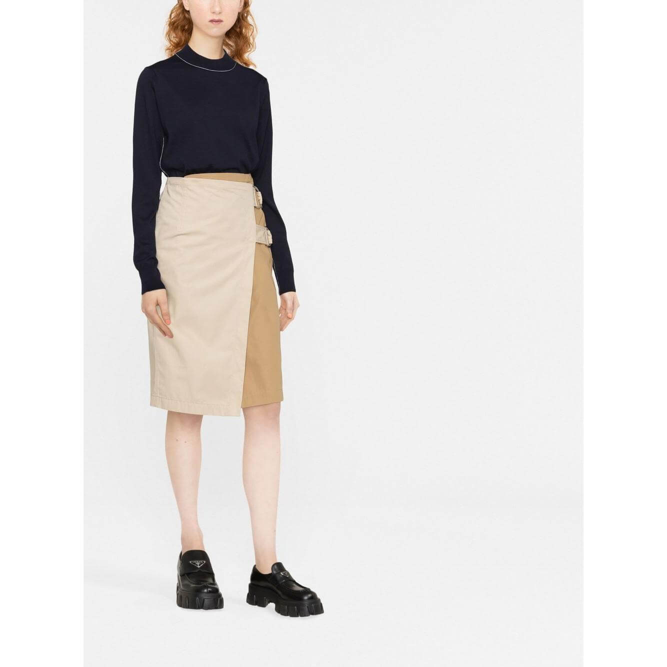 Woman wearing a navy blue Maison Margiela wool sweater with frayed detailing and a beige skirt featuring buckle accents.