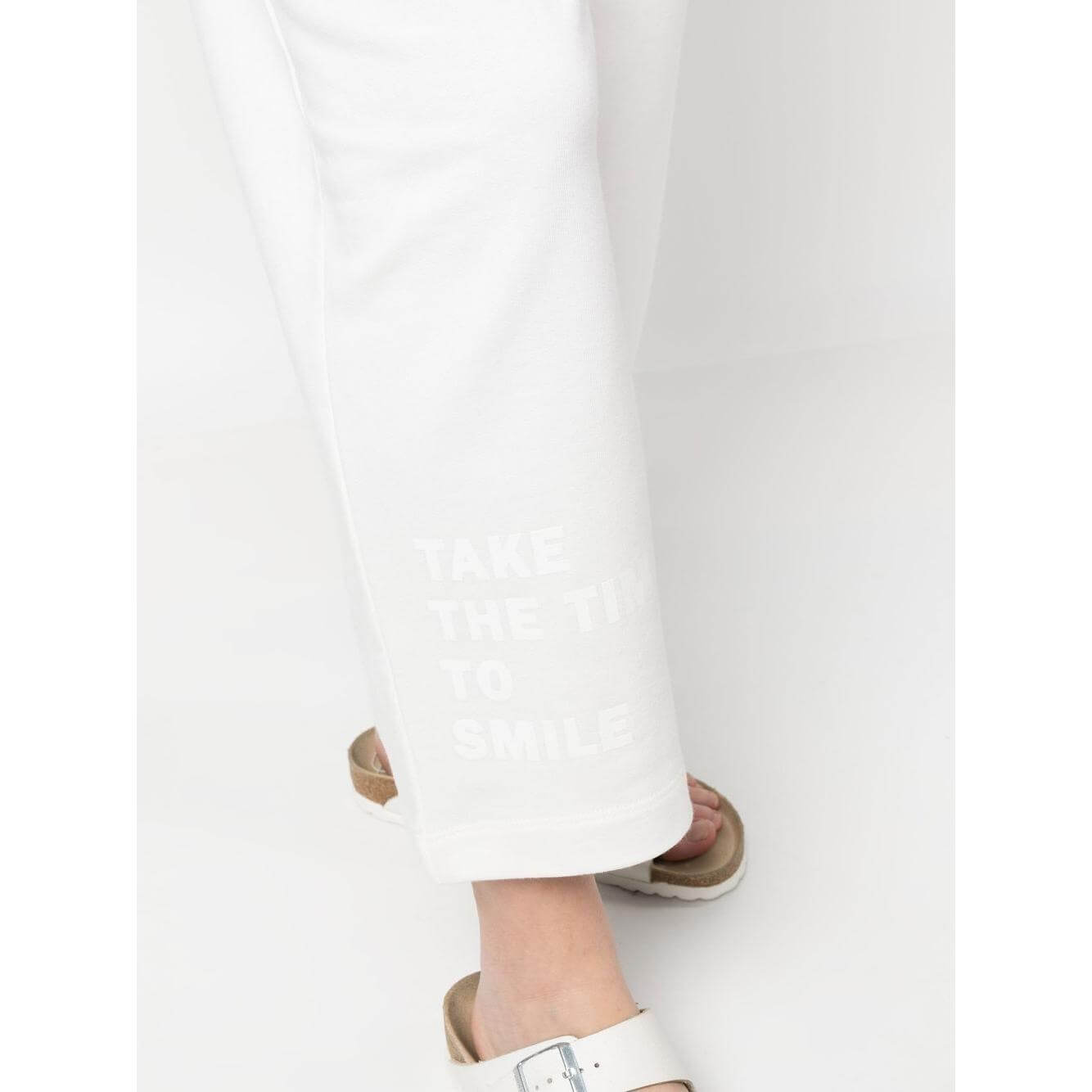 Close-up of Joshua Sanders white trousers with print detail, featuring elastic waistband and casual sandals, emphasizing comfort and style.