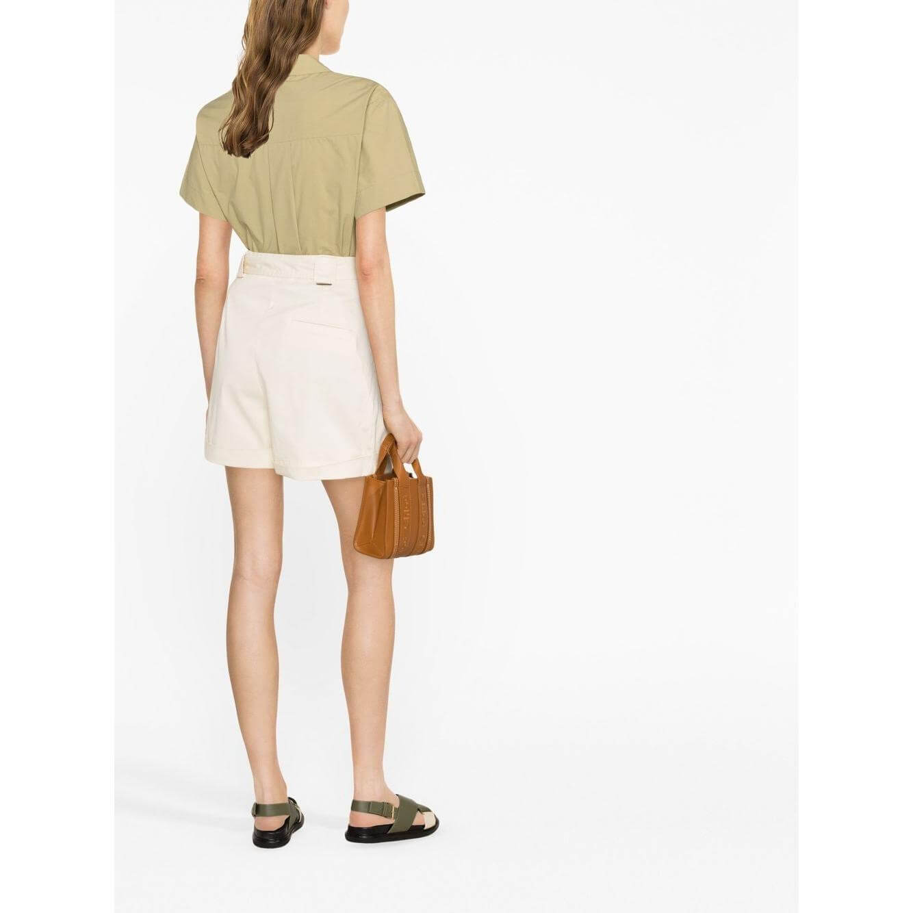 Back view of person wearing Woolrich beige tied-waist cotton shorts with turn-up hem, holding a brown handbag, standing indoors.