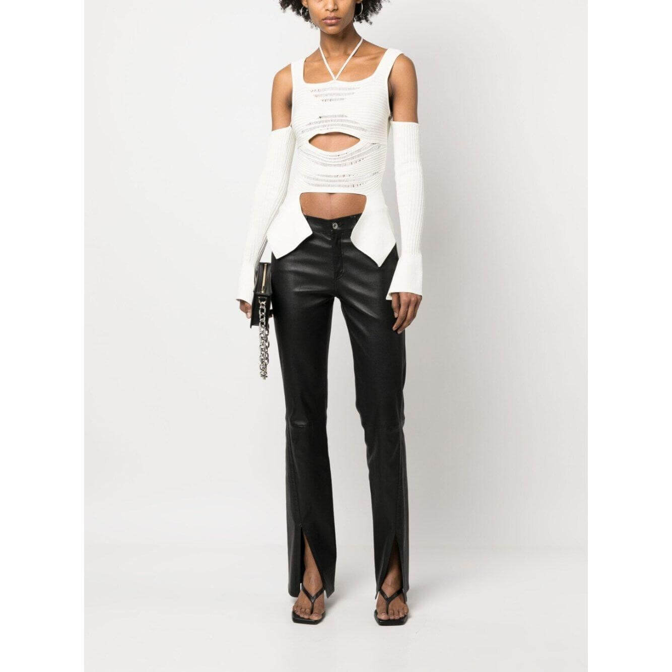 Woman wearing Andrea Adamo white cut-out ribbed knit top with wide straps and halterneck, paired with black pants.