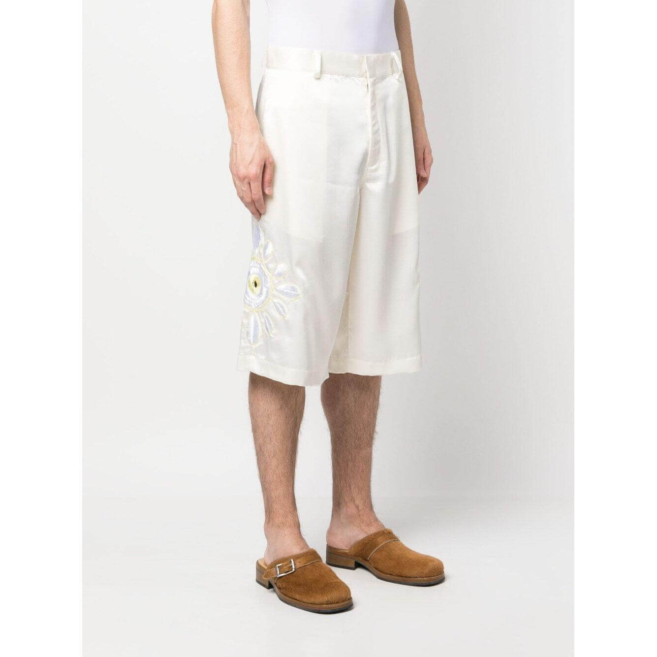 Man wearing BLUEMARBLE cream white embroidered satin shorts with belt loops, knee-length cut, and side pockets