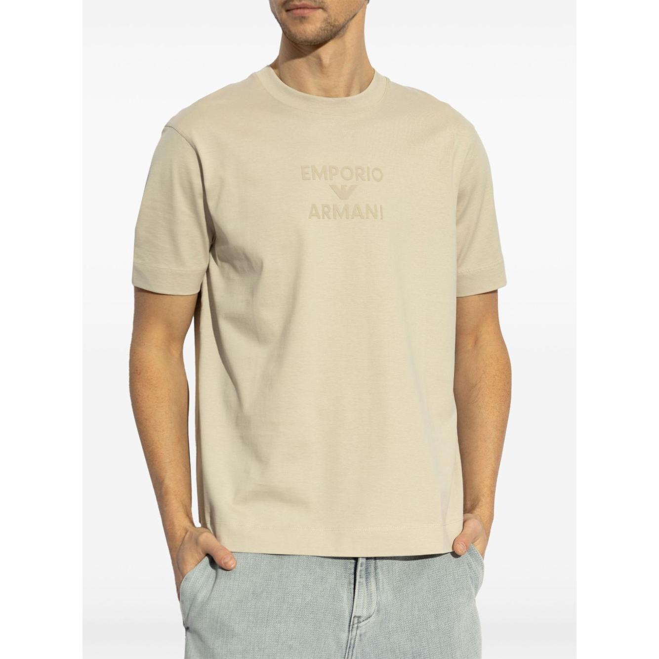 Man wearing Emporio Armani beige crew neck T-shirt with embossed logo, short sleeves, straight hem, paired with jeans.