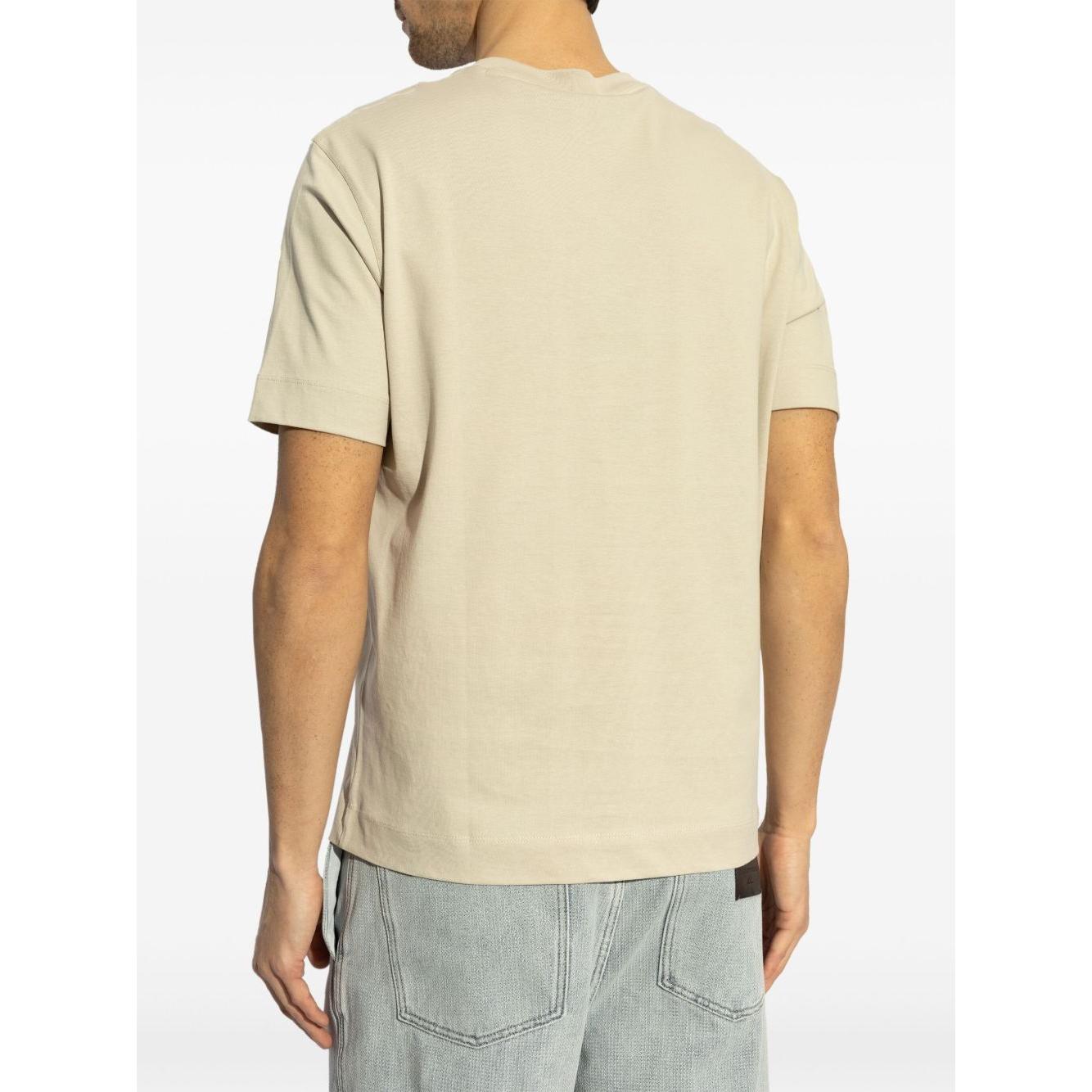 Back view of a beige Emporio Armani logo printed T-shirt with short sleeves, worn by a model in light denim jeans.
