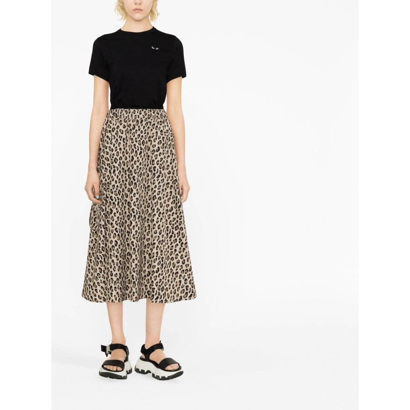 Model wearing Comme des Garçons Play black T-shirt with heart logo, paired with leopard print skirt and sandals.