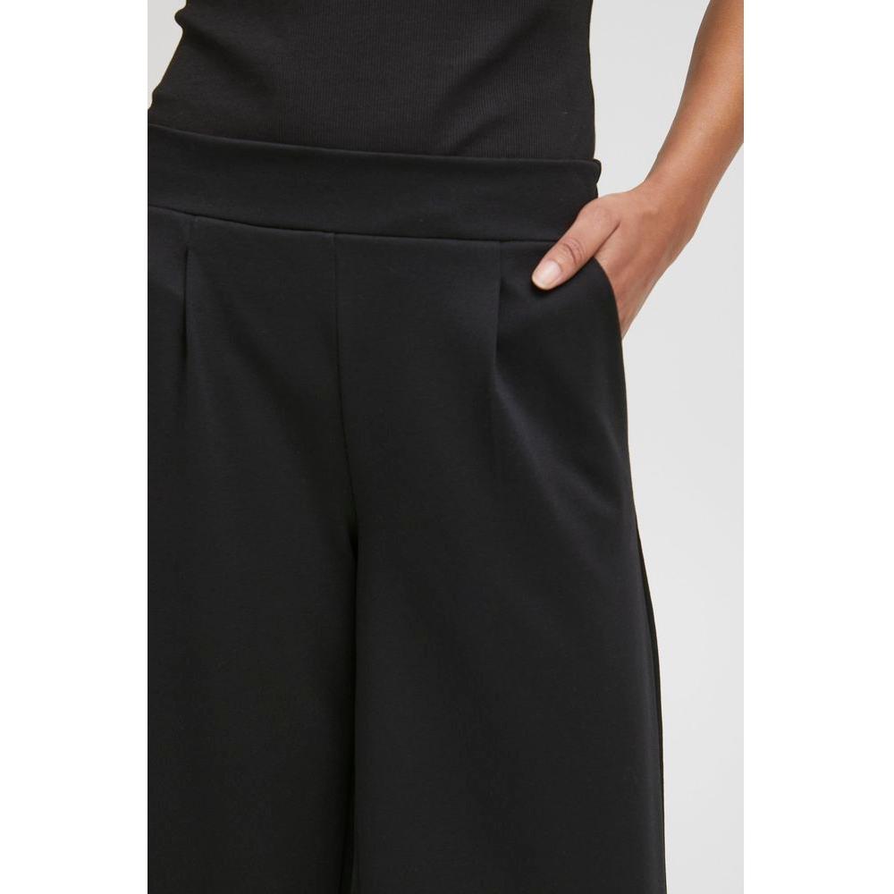 Woman wearing ICHI black bootcut pants made of recycled polyester fabric, showcasing a hand in pocket detail.