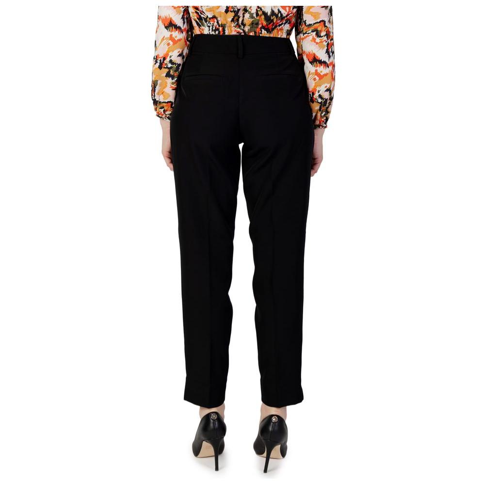 Rear view of women's black cigarette pants made from recycled polyester, part of autumn/winter collection, worn with patterned blouse.