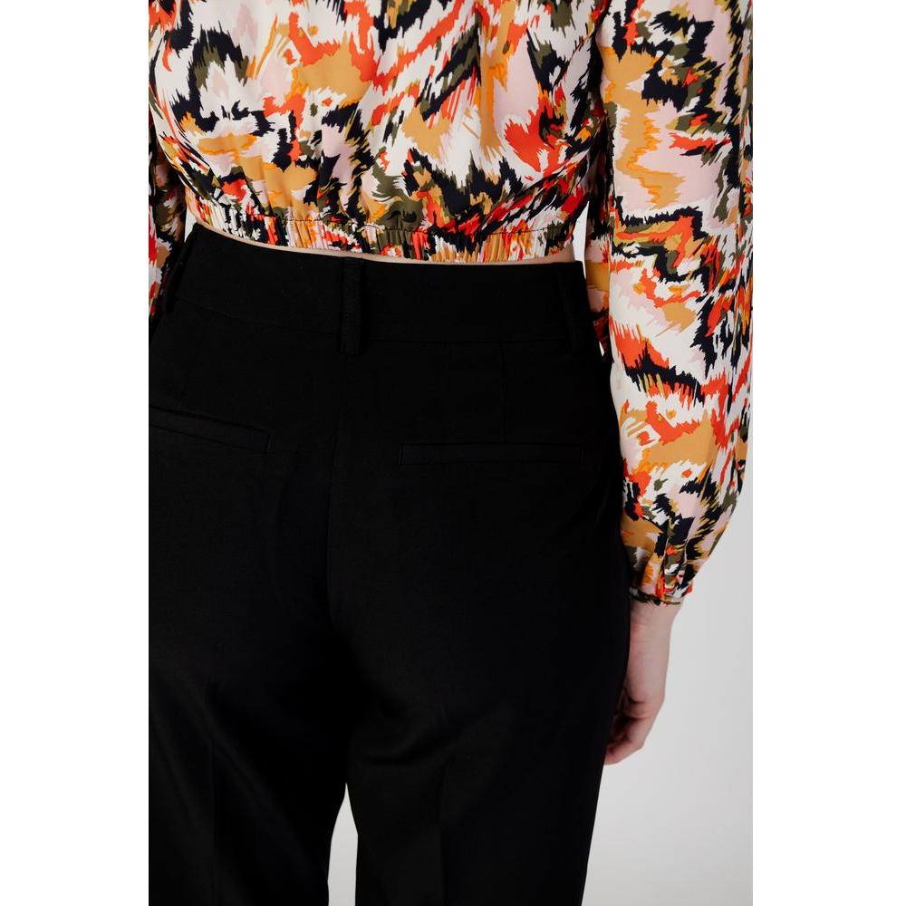 Back view of women's black recycled polyester cigarette pants from Autumn/Winter collection paired with a colorful patterned top.