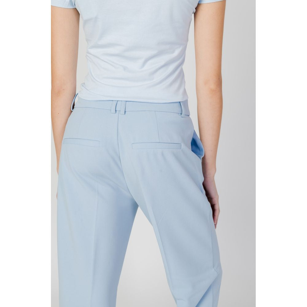 Woman wearing light blue polyester cigarette pants, back view, spring/summer collection.