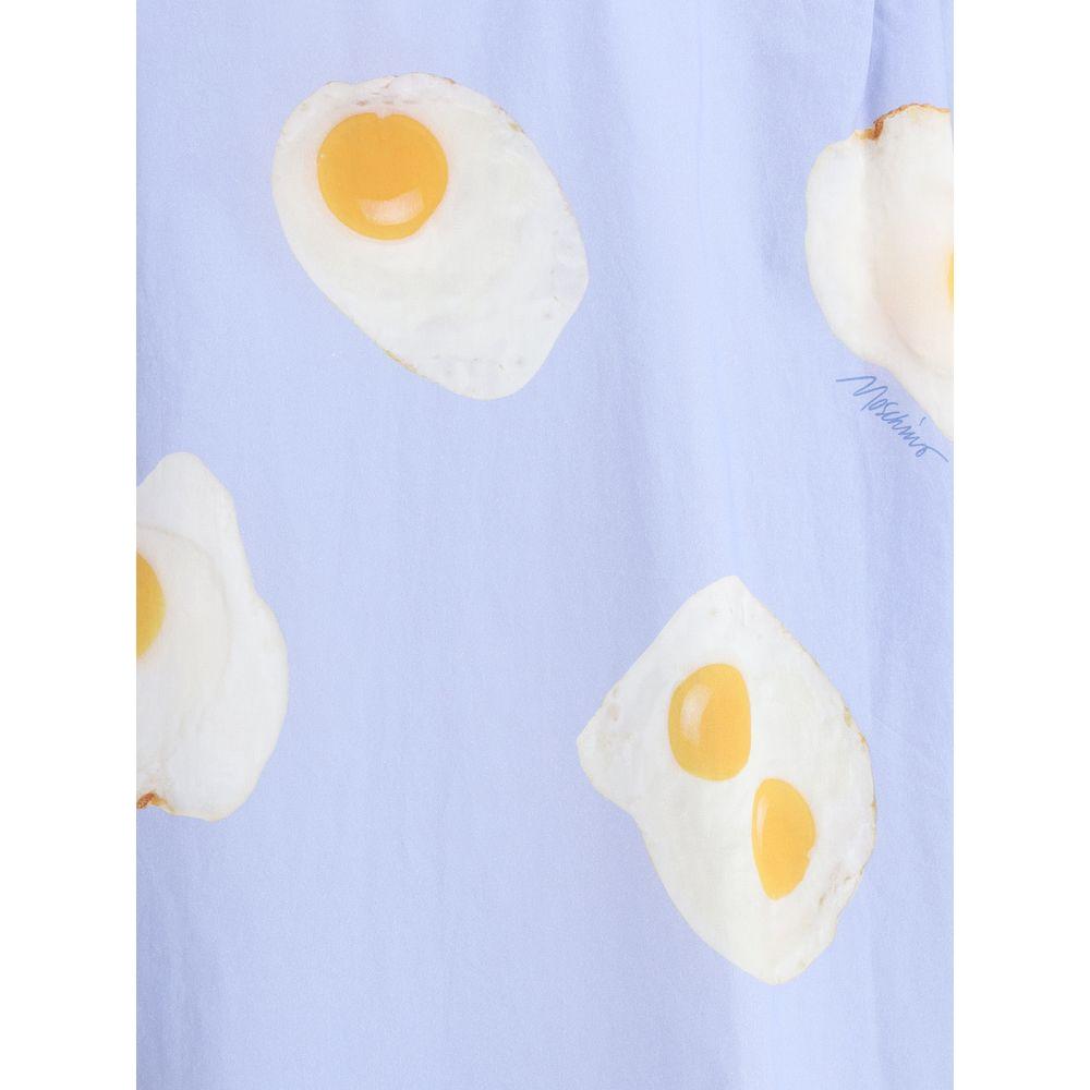 Moschino shirt with playful fried egg print on pastel blue fabric, showcasing the brand's ironic and creative style.