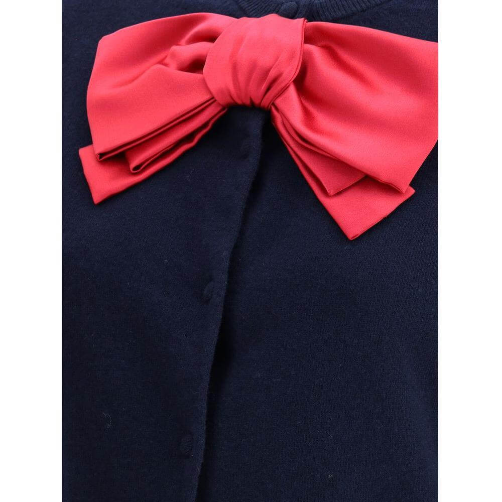 Valentino Bow Cardigan with red satin bow on navy fabric, featuring ribbed neck and button closure for elegance and comfort.