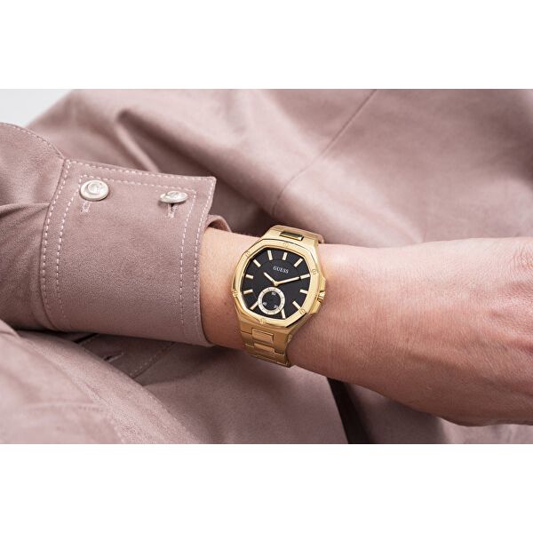 Man wearing GUESS Mod. GW0310L2 watch on wrist, gold and black design, quartz movement, displayed against light pink sleeve.