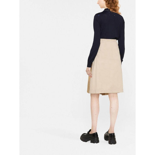 Back view of woman wearing a beige skirt and black long-sleeve top with chunky shoes on white background.