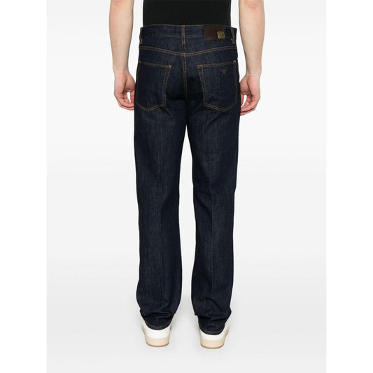 Back view of a model wearing indigo blue Emporio Armani tapered jeans with classic five pockets and rear logo patch.