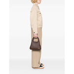 Person holding Coach Lana 25 leather crossbody bag in coffee brown, featuring top handles and adjustable strap.