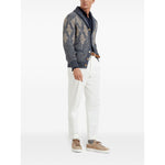 Man wearing a stylish button-up cardigan with pattern, navy shirt, white trousers, and tan sneakers, standing against a plain background.