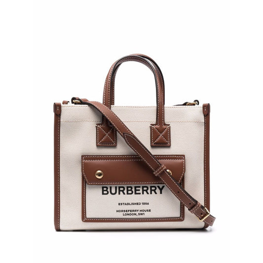 Burberry mini tote bag in cream cotton with brown leather trim, logo print, and gold-tone hardware, featuring adjustable shoulder strap and handles.
