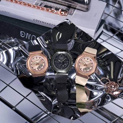 Three CASIO G-SHOCK Mod. MINI OAK G-STEEL watches on reflective surface, showcasing design and color variations, with official packaging.