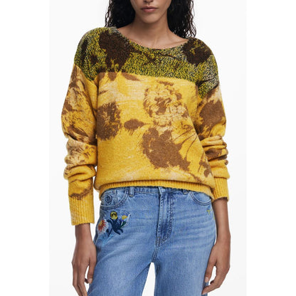 Model wearing Desigual Yellow Wool Women Sweater, featuring vibrant floral patterns and crew neck, paired with blue jeans.