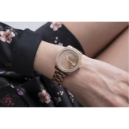 Stylish woman wearing GUESS Mod. GW0307L3 quartz watch, rose gold finish with calendar, 36 mm case, floral dress background.