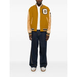 Man wearing a Golden Goose Coats varsity-style bomber jacket with mustard yellow leather sleeves, letter patch, and ribbed trims.