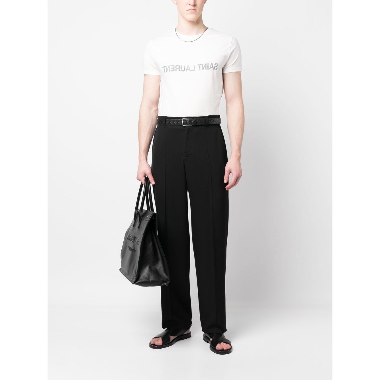 Model wearing Saint Laurent Logo T-shirt with black pants, carrying a black bag, displaying the reverse logo print design.