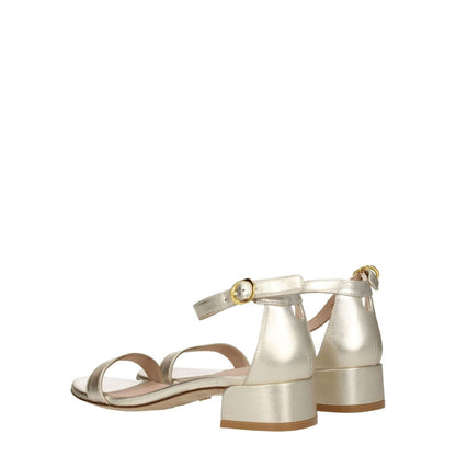 Stuart Weitzman Gold Leather Sandals with buckle closure and mid heels, showcasing an open toe design in metallic platinum color.