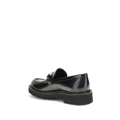 Valentino Garavani Black Leather Slip-On Loafers with VLogo brass detail, showcasing rubber lug sole for stability and comfort.